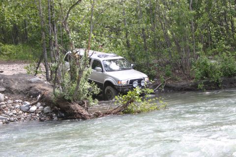 2003 Jeep TJ - A Toyota Tacoma navigates a rocky riverbed surrounded by dense foliage.