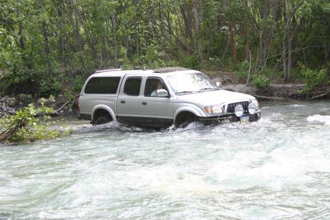 2003 Jeep TJ - Silver Toyota Tacoma pickup truck navigates a river crossing surrounded by trees.