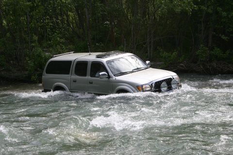 2003 Jeep TJ - A silver Toyota Tacoma navigates through a fast-moving river surrounded by trees.