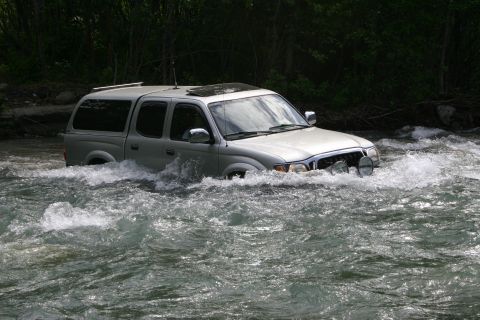 2003 Jeep TJ - A silver pickup truck navigates through a fast-flowing river, its front end partially submerged in the water.