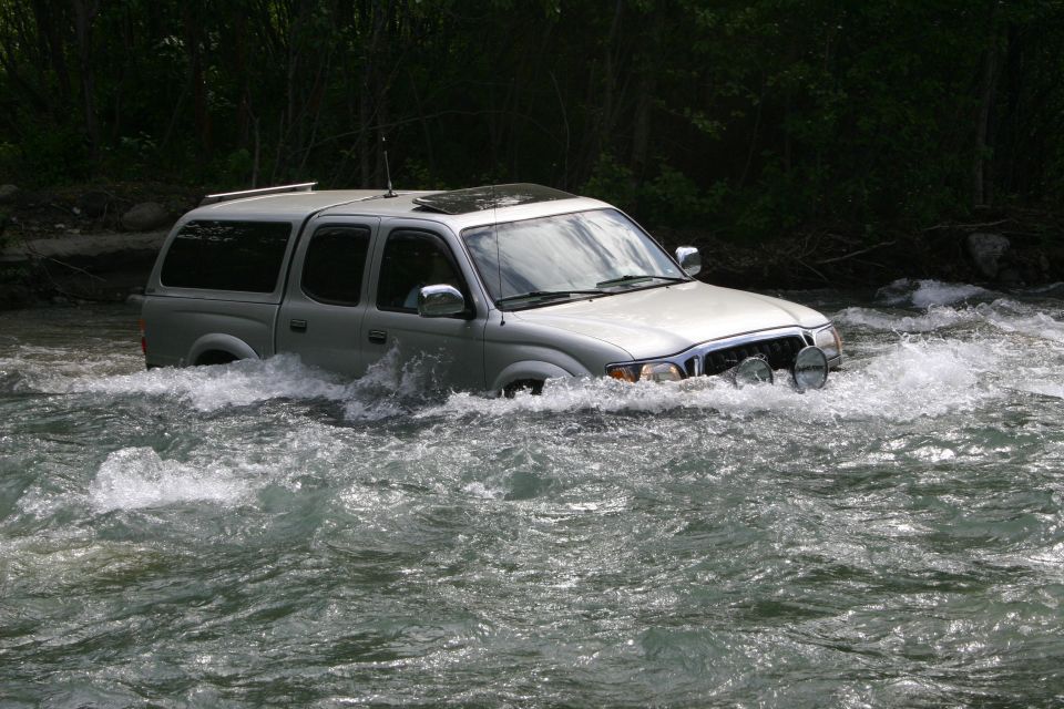 Silver pickup truck driving through a river with aftermarket lights