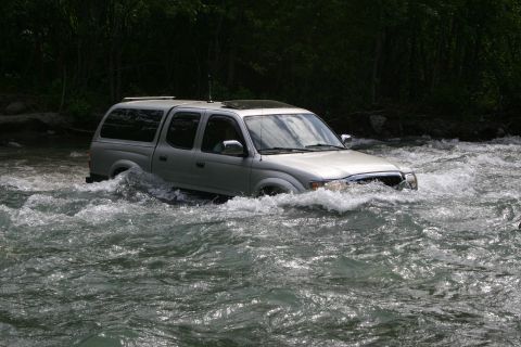 2003 Jeep TJ - Silver Toyota Tacoma pickup truck with a camper shell navigates a river.