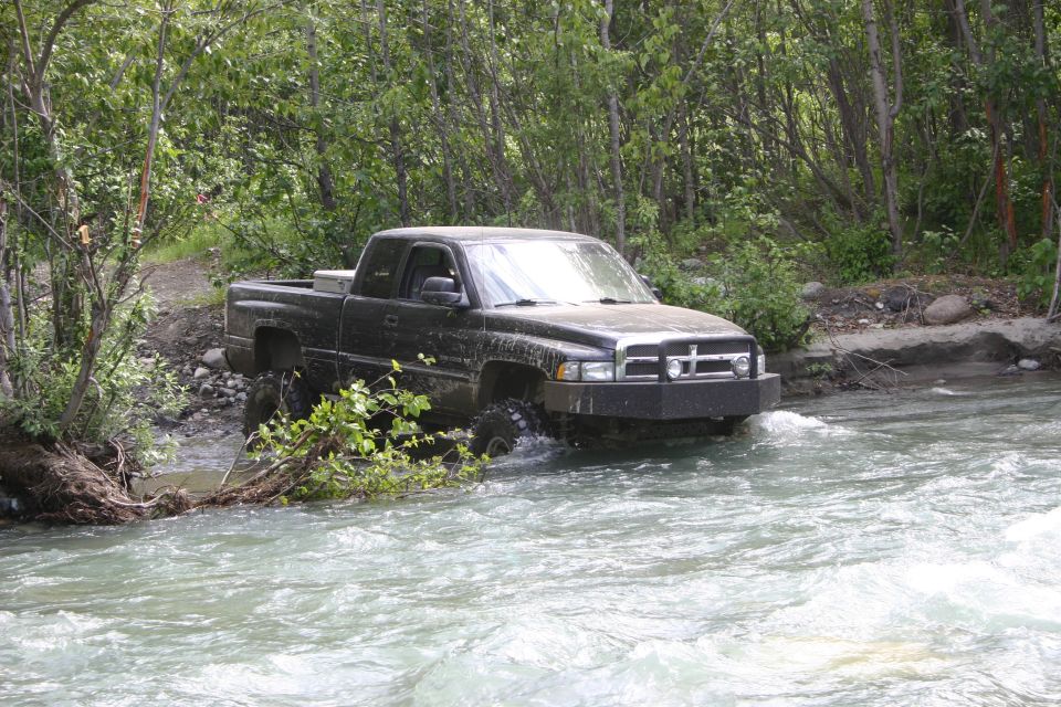 Black pickup truck driving through a shallow river with trees on the bank