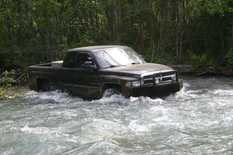 2003 Jeep TJ - This black Dodge Ram pickup truck is navigating through a river, surrounded by dense foliage.