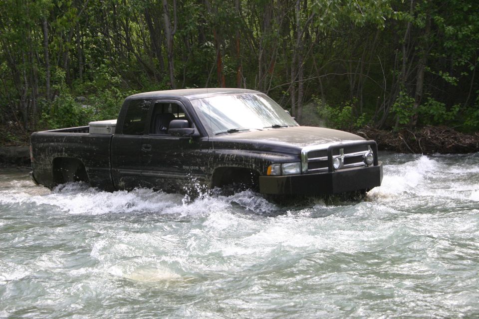 Black Dodge Ram pickup truck driving through a river. It has a toolbox in the bed and a brush guard on the front