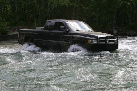 2003 Jeep TJ - A black pickup truck navigates through a fast-flowing river, kicking up water.