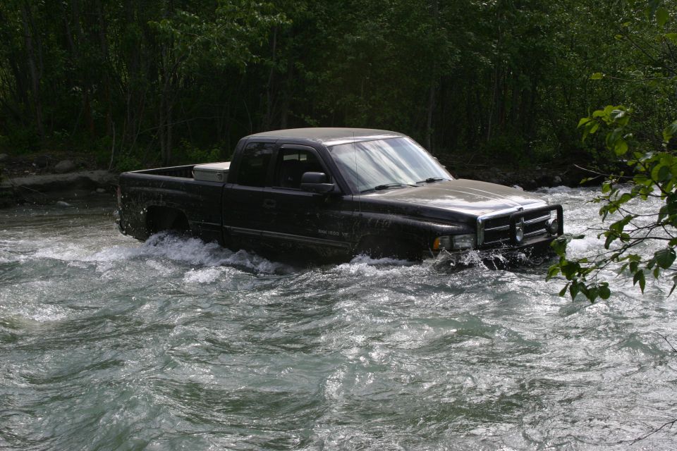 Black Dodge Ram pickup truck crossing a river, water splashing around it
