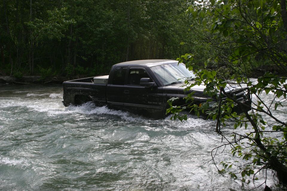 Black Dodge Ram pickup truck driving through a fast-moving river, trees on both sides