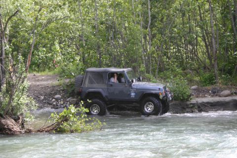 2003 Jeep TJ - Jeep TJ navigates a rocky riverbed surrounded by dense foliage.