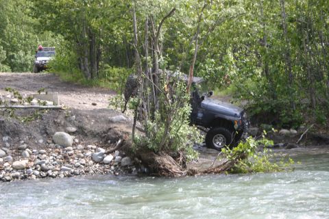 2003 Jeep TJ - Two Jeeps navigate a wooded area with a river or stream nearby.