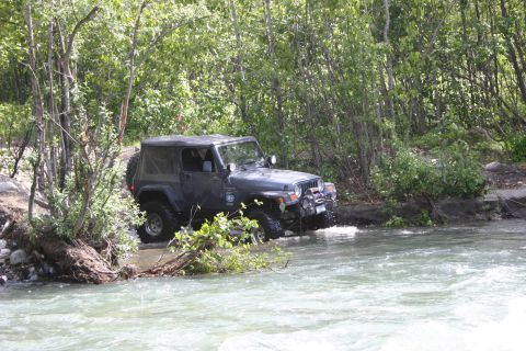 2003 Jeep TJ - A 2003 Jeep TJ navigates a rocky river crossing surrounded by dense foliage.