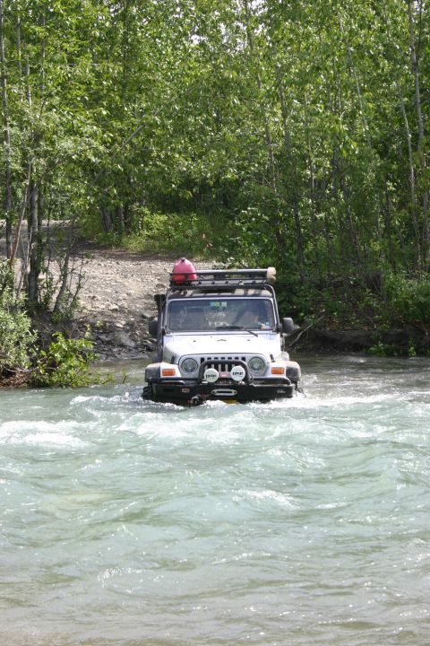 2003 Jeep TJ - A silver Jeep TJ navigates a shallow river with trees lining the banks.