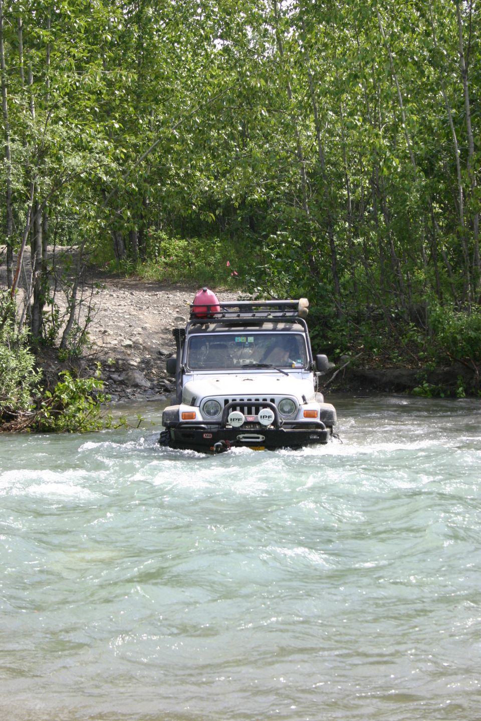Silver Jeep TJ crossing a river, with a red jerry can on its roof rack