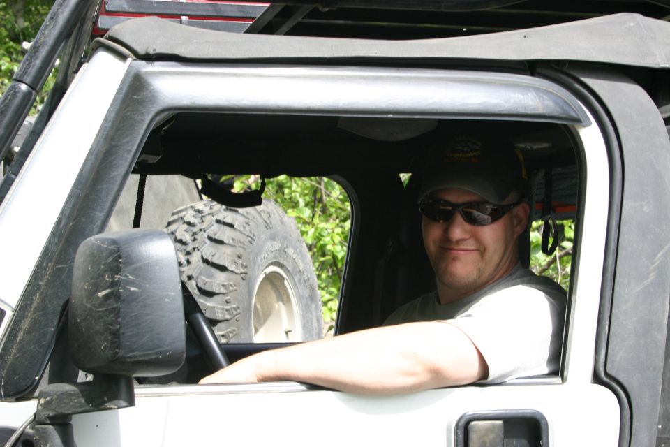 Man wearing sunglasses and a baseball cap sits in the driver's seat of a white Jeep TJ