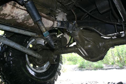 2003 Jeep TJ - The undercarriage of a heavily used 4x4 vehicle shows mud and wear on its drivetrain components.