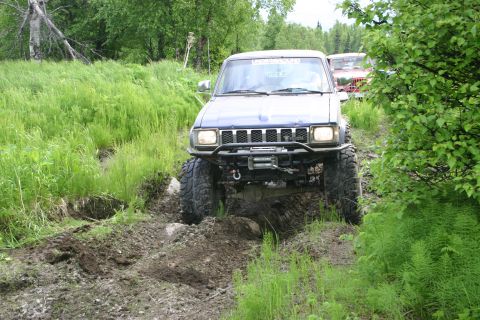 2003 Jeep TJ - An off-road SUV with a winch tackles a muddy trail, with another vehicle following in the background.