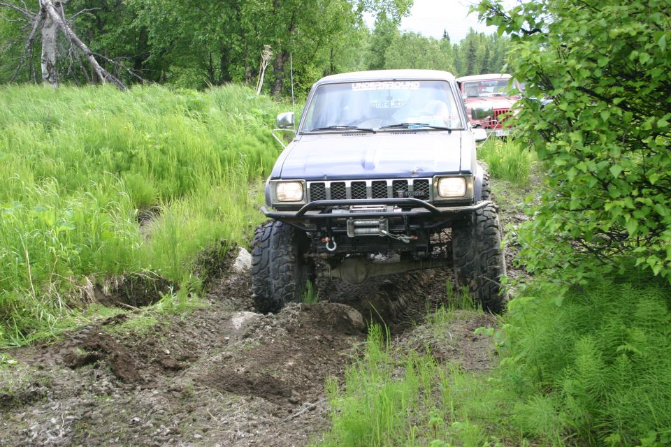Blue off-road SUV with winch navigating muddy terrain, another vehicle visible behind