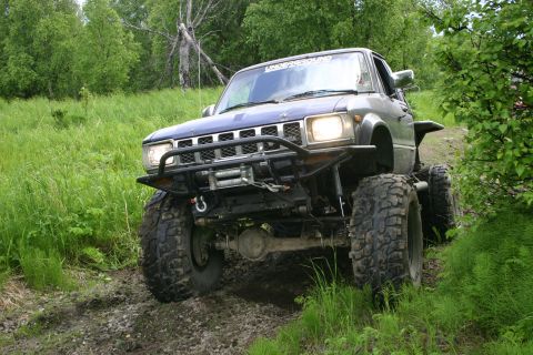 2003 Jeep TJ - Modified pickup truck with large tires and winch navigates a muddy trail.