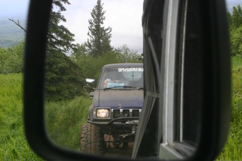 2003 Jeep TJ - A blue SUV with off-road tires is viewed through a side mirror, with another vehicle partially visible.