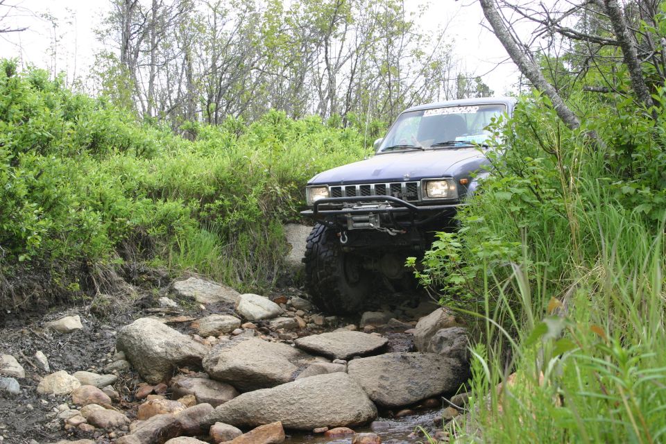 Blue SUV with winch bumper driving over rocks on a trail. Grille suggests 1990s model