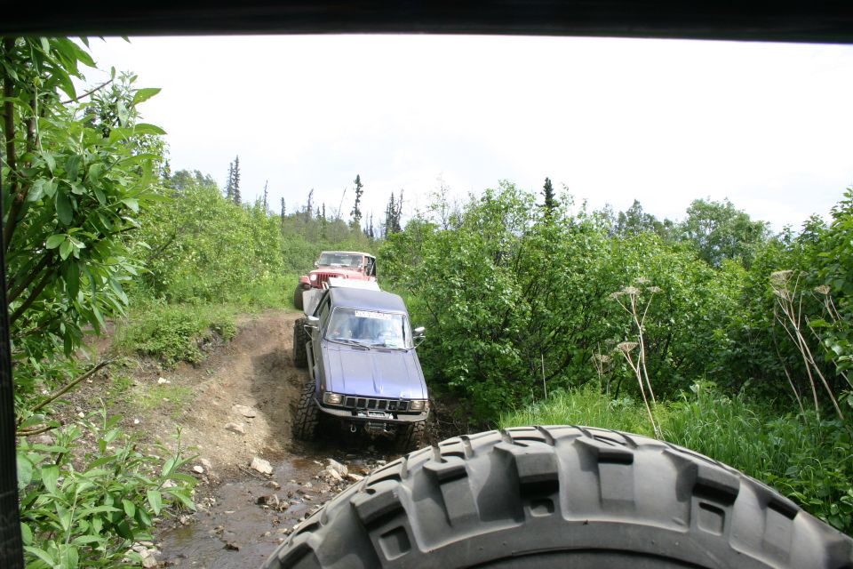 Several off-road vehicles driving on a dirt trail through a wooded area