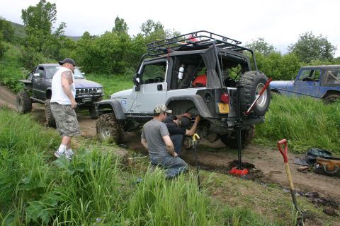 2003 Jeep TJ - A group of off-road enthusiasts work on a vehicle on a dirt trail surrounded by lush greenery.