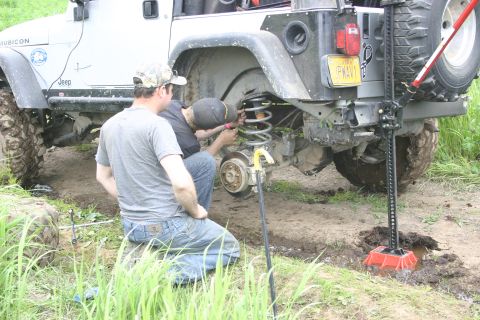 2003 Jeep TJ - Two men work on the suspension of a white Jeep Wrangler TJ, which is supported by a high-lift jack.