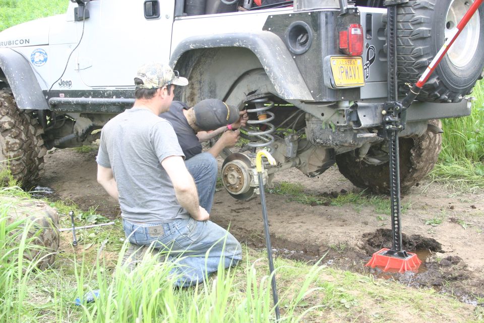 White Jeep Wrangler TJ with a yellow license plate, undergoing repair with a high-lift jack