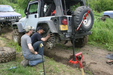 2003 Jeep TJ - Two men work on the suspension of a 2003 Jeep TJ during an off-road event in Alaska, with another vehicle visible in the background.