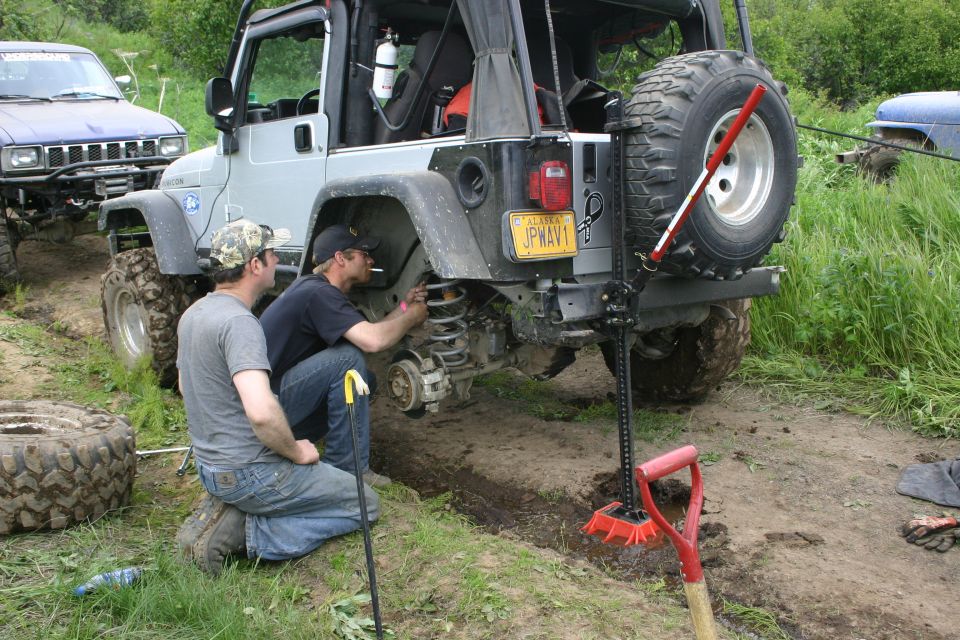 2003 Jeep TJ rear view with two men working on suspension, Alaska license plate visible