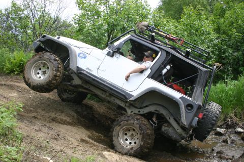 2003 Jeep TJ - A white 2003 Jeep Wrangler Rubicon tackles a challenging off-road course, demonstrating its 4x4 capabilities on a steep, muddy trail.
