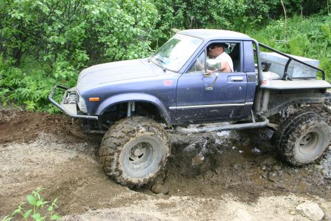 2003 Jeep TJ - A blue pickup truck navigates a challenging muddy terrain.
