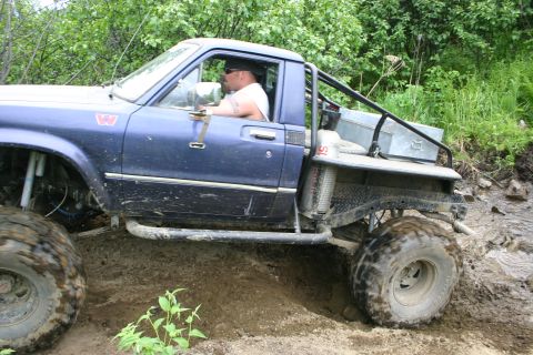 2003 Jeep TJ - This modified pickup truck is shown off-roading on a dirt trail with large, aggressive tires.