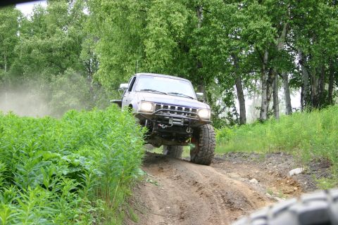 2003 Jeep TJ - A modified pickup truck navigates a dusty trail through a wooded area.