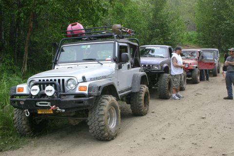 2003 Jeep TJ - Several modified off-road vehicles, including a silver Jeep TJ, are parked on a dirt path.