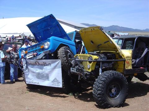 1986 Ford Bronco II - A blue 1986 Ford Bronco and a yellow Jeep are displayed with their hoods open at an outdoor event.