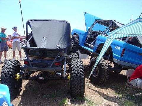 1986 Ford Bronco II - Two custom off-road vehicles are displayed outdoors, one with its hood open.