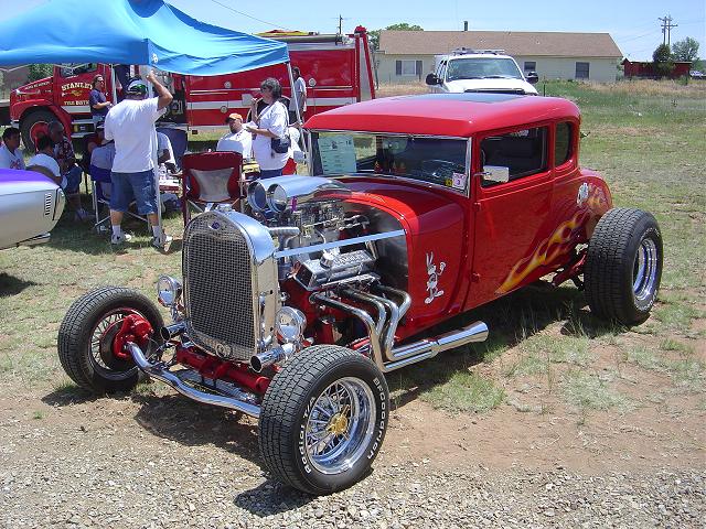 Red hot rod coupe with flames and a V8 engine, viewed from the front three-quarter angle