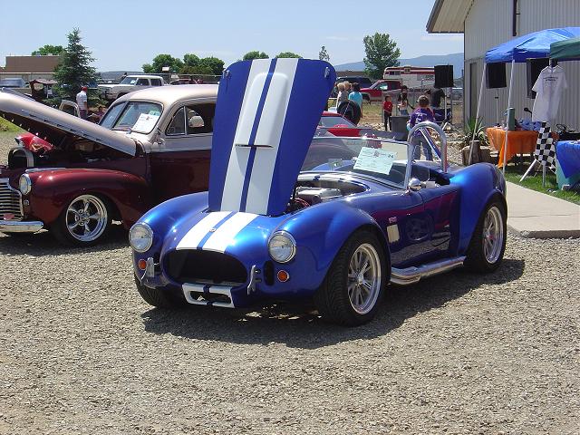 Blue AC Cobra replica with hood open, parked next to a maroon classic car