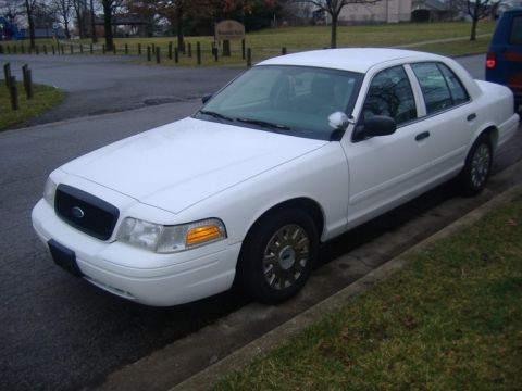 2003 Ford Crown Victoria - A white 2003 Ford Crown Victoria is parked on the side of the road next to a grassy area.