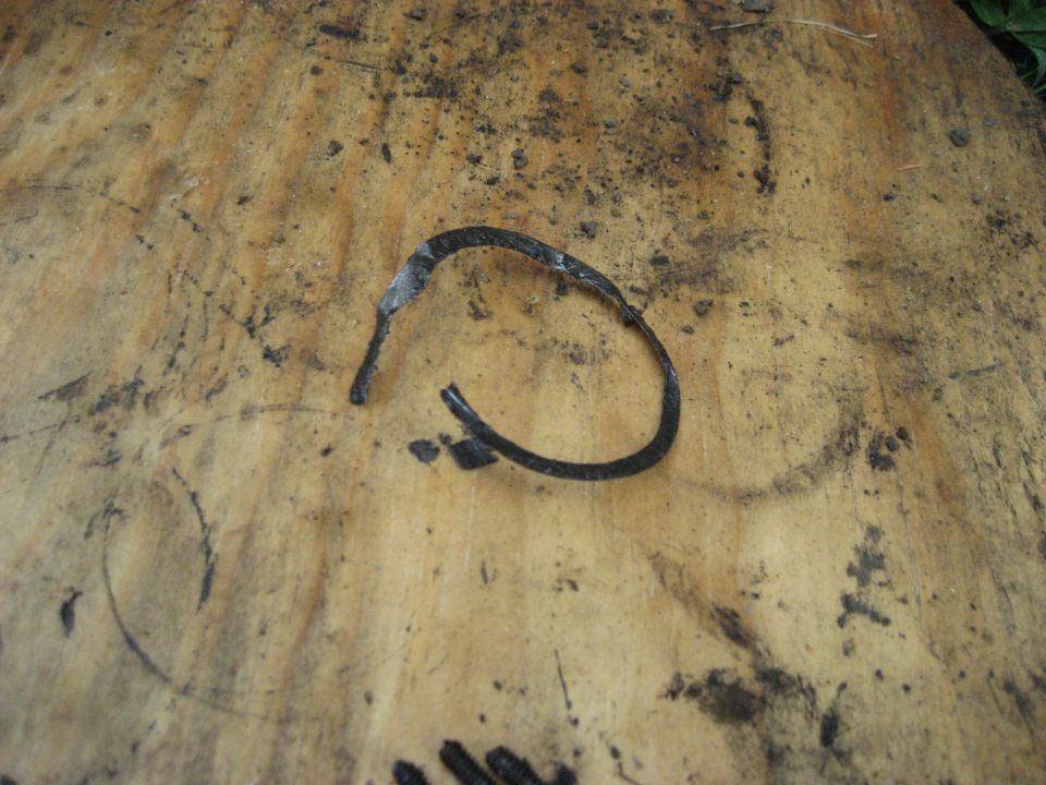 Black wire snap ring retaining clip on an oily plywood bench