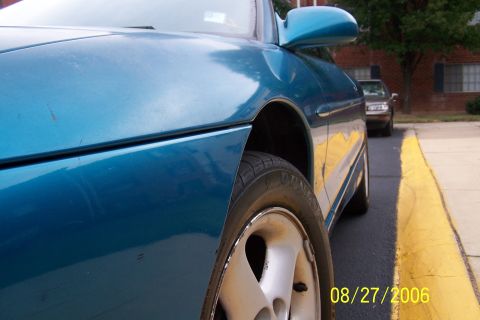 1994 Ford Probe - Close-up of a blue car's side panel and wheel, with a second vehicle visible in the distance.