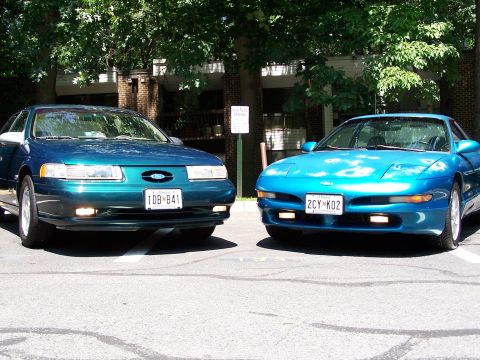1994 Ford Probe - Two Ford vehicles, a blue Probe and a teal Taurus, are parked side-by-side in a lot.