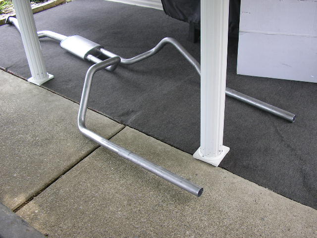 Exhaust system pipe and muffler assembly laid out on a dark mat between white posts
