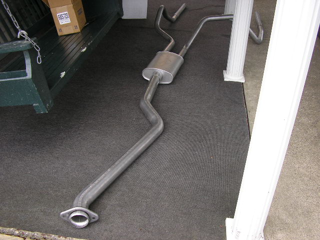 exhaust system laid out on a dark mat, with a box and part of a green bench in the background