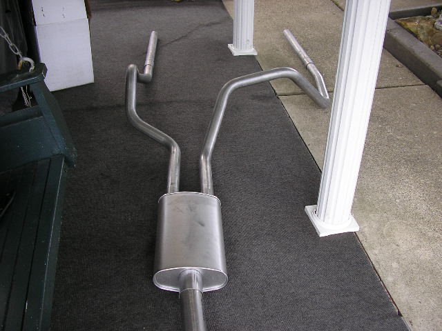 Dual exhaust system with oval muffler and bent pipes on dark carpet