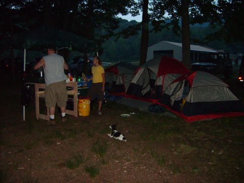 1995 Ford Bronco - A campsite scene with multiple tents set up, people preparing food, and a dog resting on the ground.