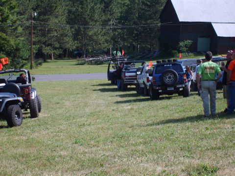 1995 Ford Bronco - A group of off-road vehicles are gathered in a field, with a barn in the background and people socializing.
