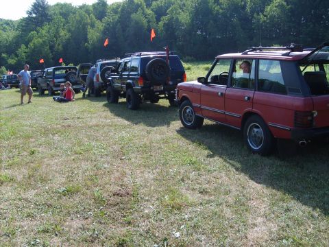1995 Ford Bronco - A red Range Rover Classic is parked in a grassy area, with other off-road vehicles lined up behind it.