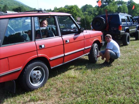 1995 Ford Bronco - Two SUVs are parked on a grassy field on a sunny day. A man is checking the front tire of the red Range Rover.